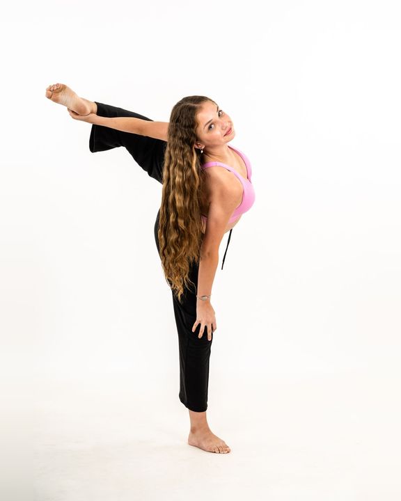 Dancer in a pink top holding her leg behind her