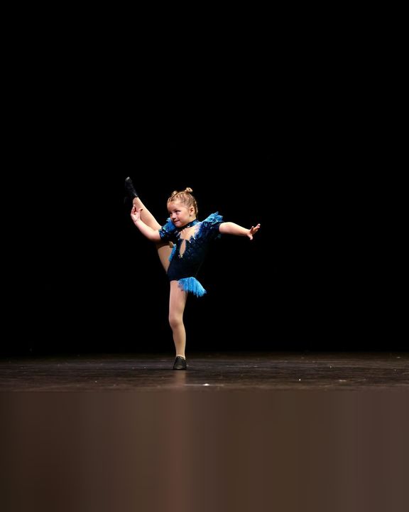 Young soloist in blue performing a leg extension on stage